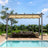 10x10 ft Beige Patioslife Atlantic retractable pergola with adjustable canopy over wicker patio seating beside a pool, garden greenery and ocean view