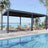 Patioslife Atlantic 10×20ft charcoal aluminium louvered pergola shading poolside loungers with palm trees and waterfront view
