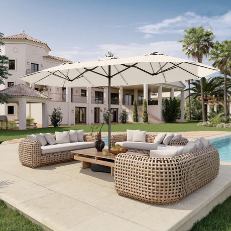 Patioslife Horizon 15 x 9 ft cream double-sided patio umbrella with base shading a poolside wicker sofa set in front of a luxury villa