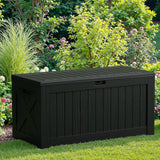 Patioslife Outdoor Resin Deck Box closed on a backyard lawn with flower beds and greenery for weatherproof garden tool and patio storage