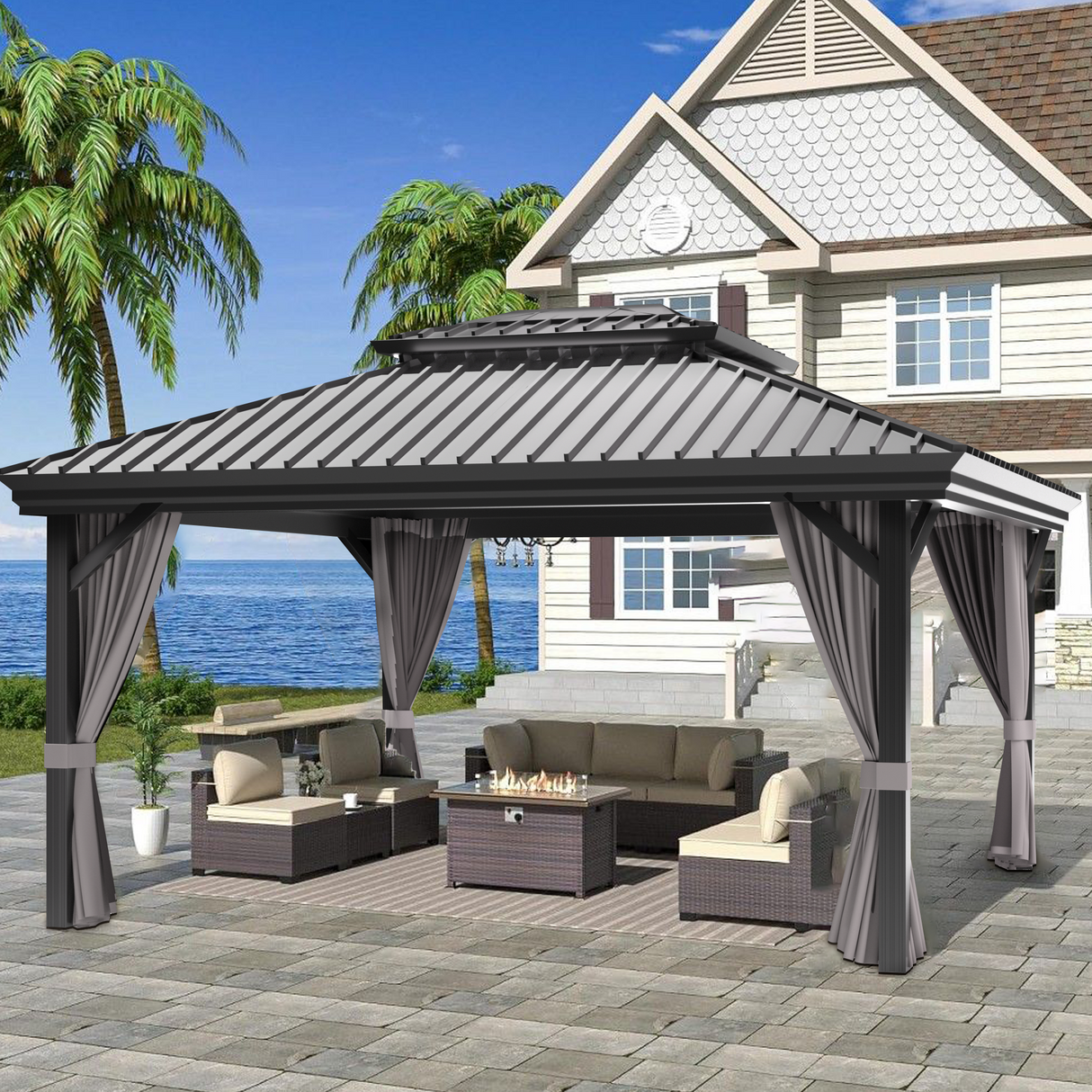Patioslife Haven 10' x 12' grey hardtop pergola gazebo with double vented roof and side curtains, set on a stone patio beside a coastal home with ocean view and outdoor sofa seating