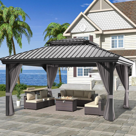 Patioslife Haven 10' x 12' grey hardtop pergola gazebo with double vented roof and side curtains, set on a stone patio beside a coastal home with ocean view and outdoor sofa seating