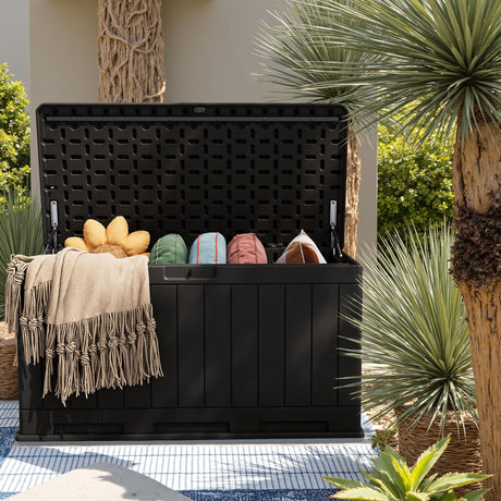 Patioslife Outdoor Resin Deck Box open with patio cushions and throw blankets in a tropical garden setting for weatherproof outdoor storage